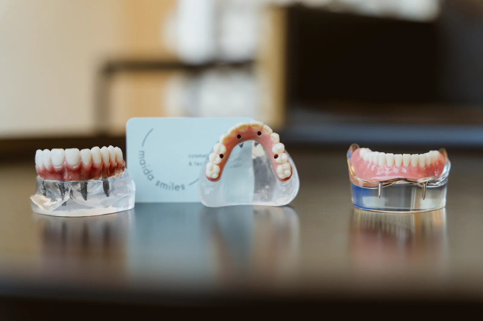 Three implant-supported dental models are arranged on a clinic table.