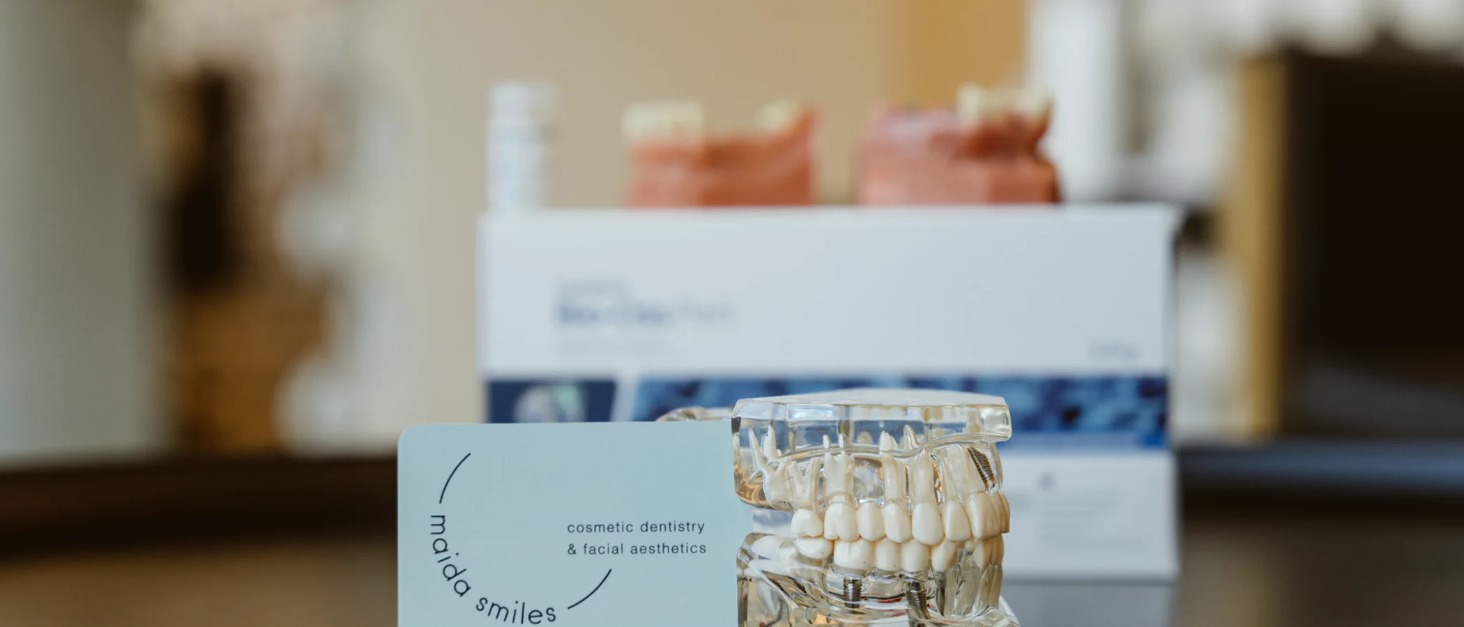 A clear dental model shows implant-supported teeth against a Maida Smiles clinic backdrop.
