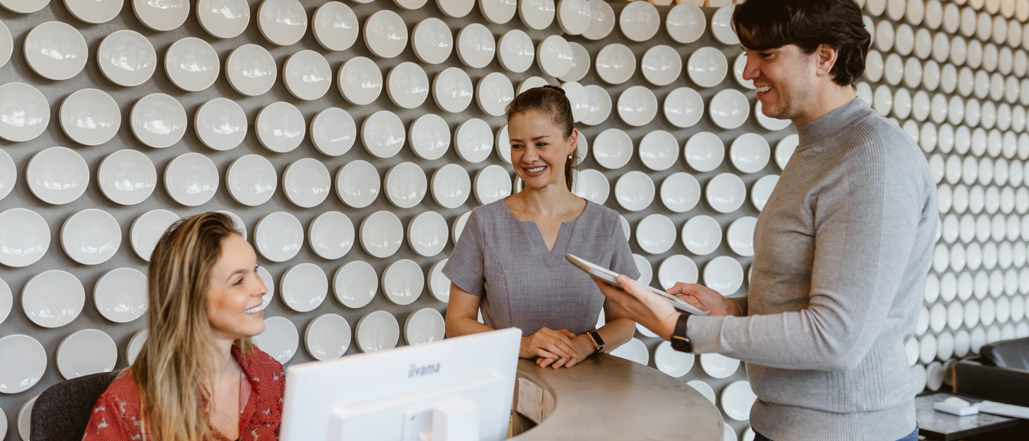 Maida Smiles staff welcome a patient at the curved reception desk.
