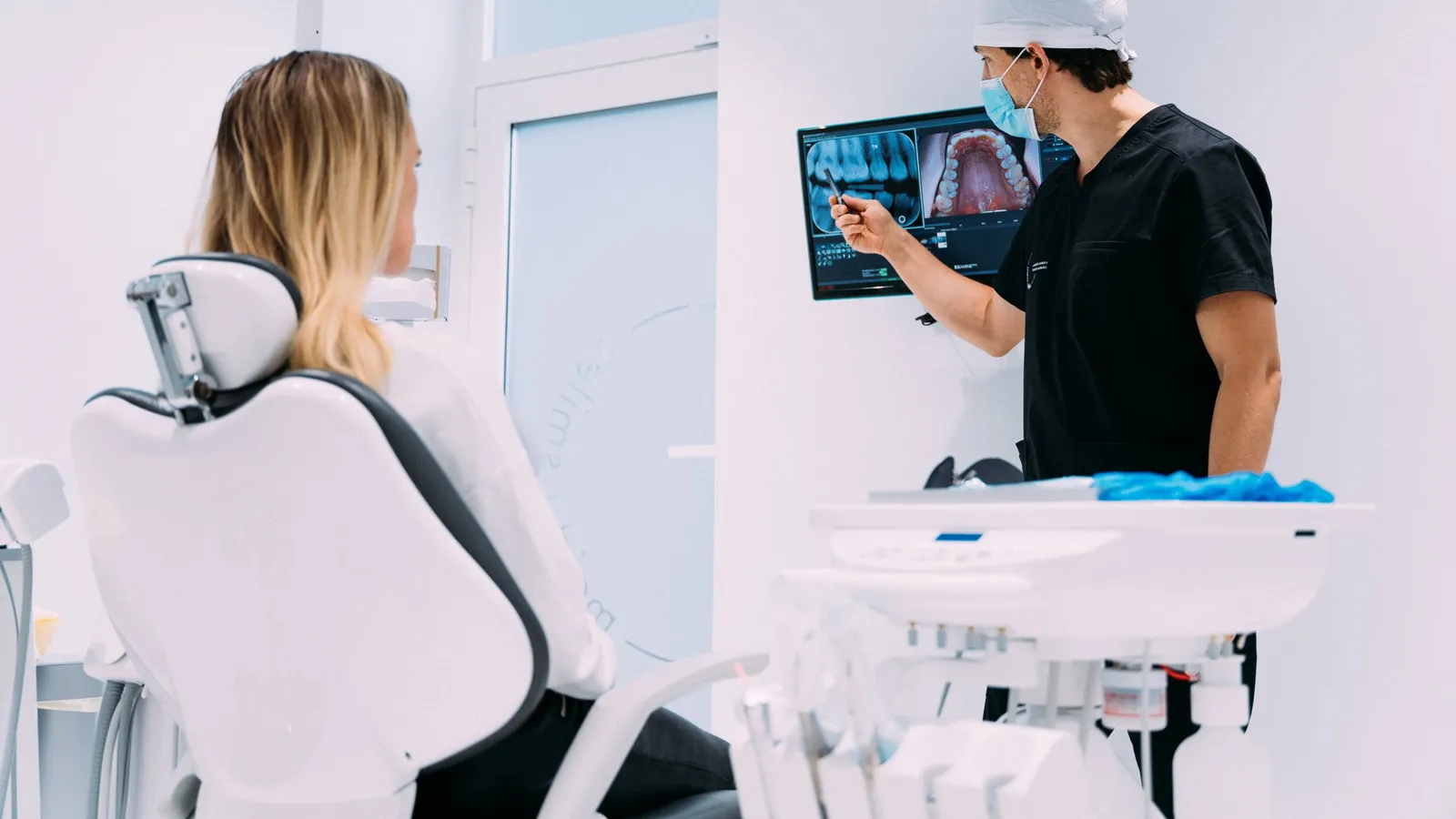 Dentist explaining dental scans and X-ray images to a seated patient in a treatment room