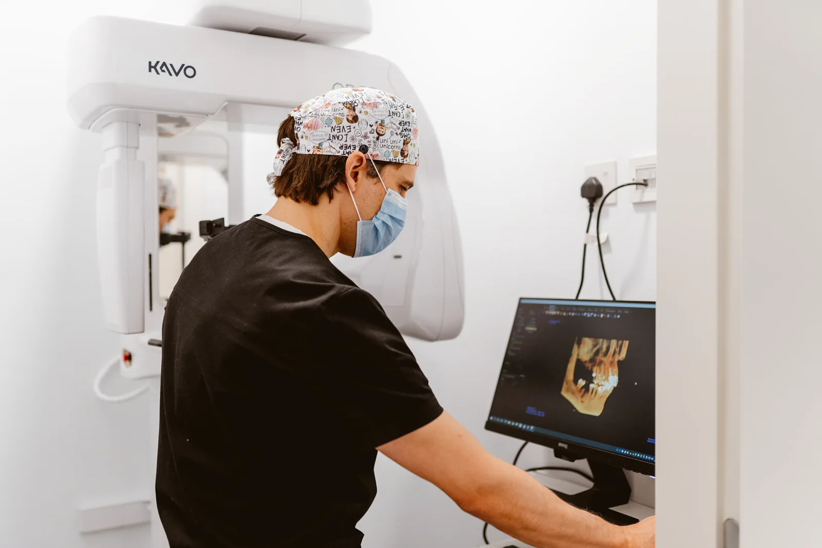 A clinician reviews a 3D jaw scan beside the CBCT unit.