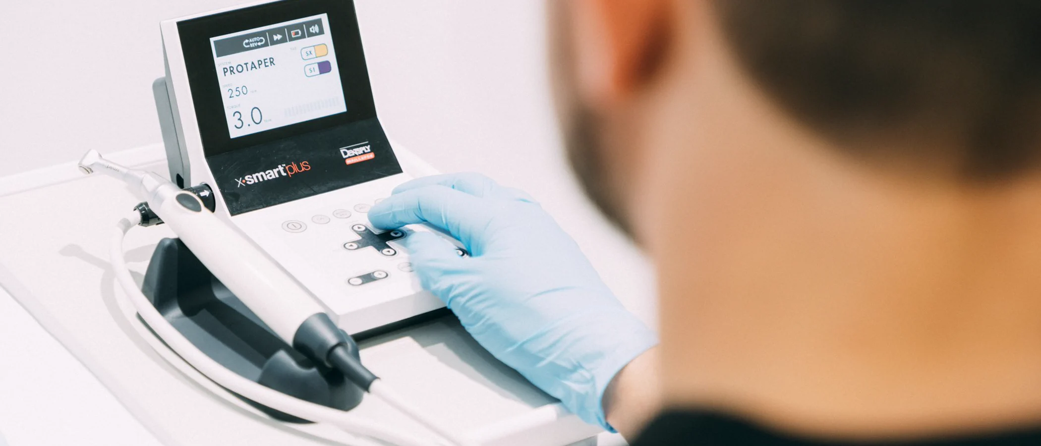 A gloved dentist uses an endodontic motor during root canal treatment.