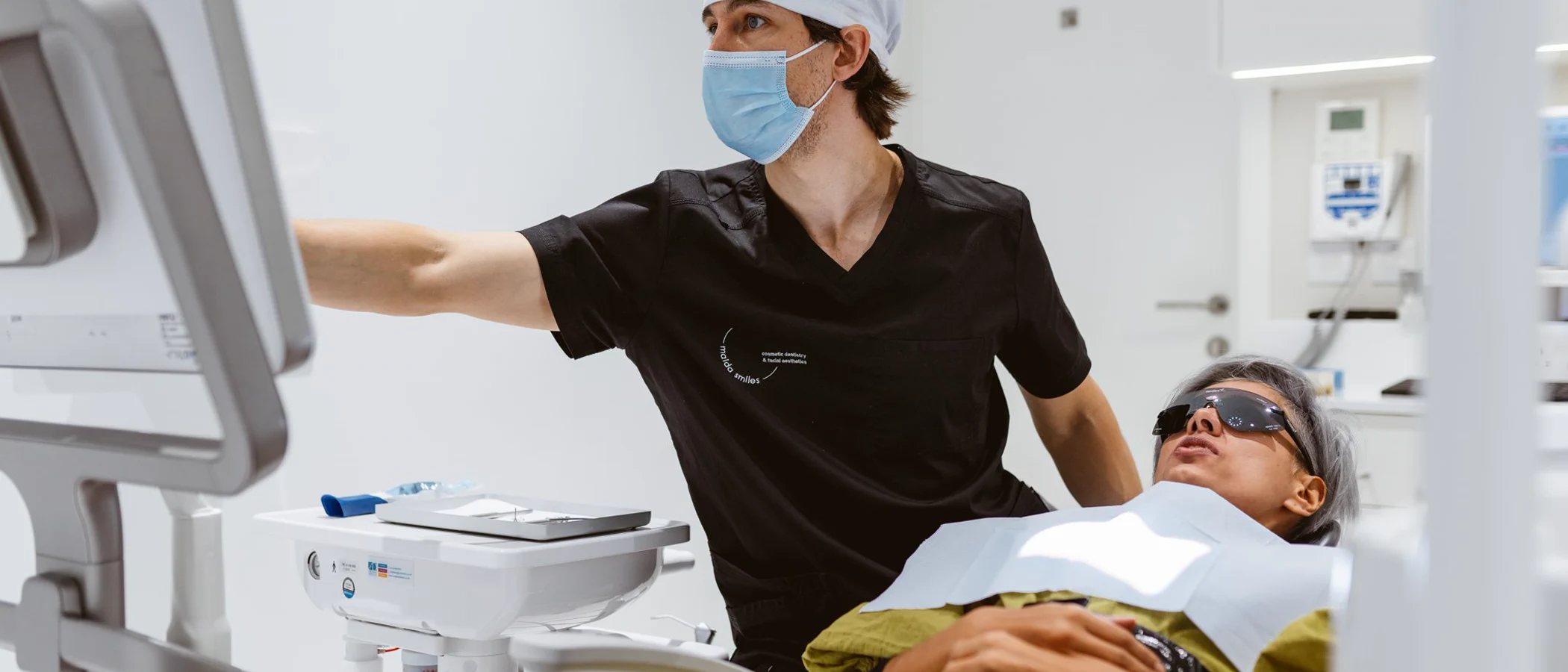 A Maida Smiles practitioner stands beside a patient in a bright treatment room.
