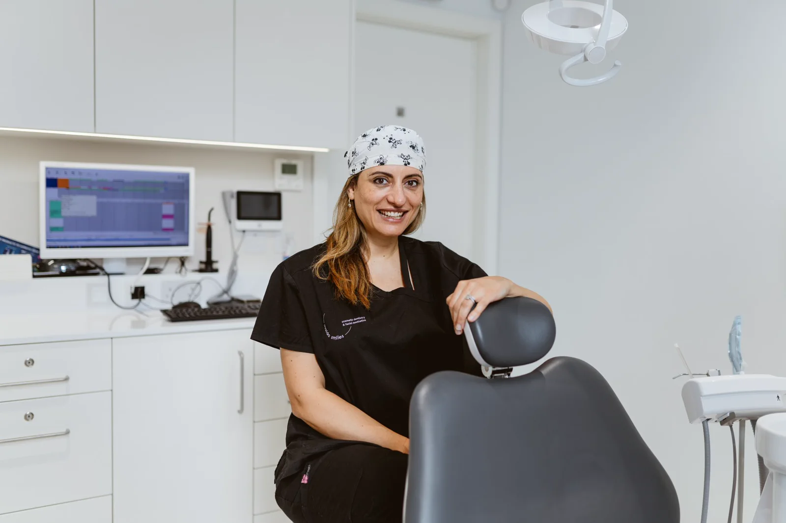 A clinician smiles beside the dental chair in a calm, modern surgery.