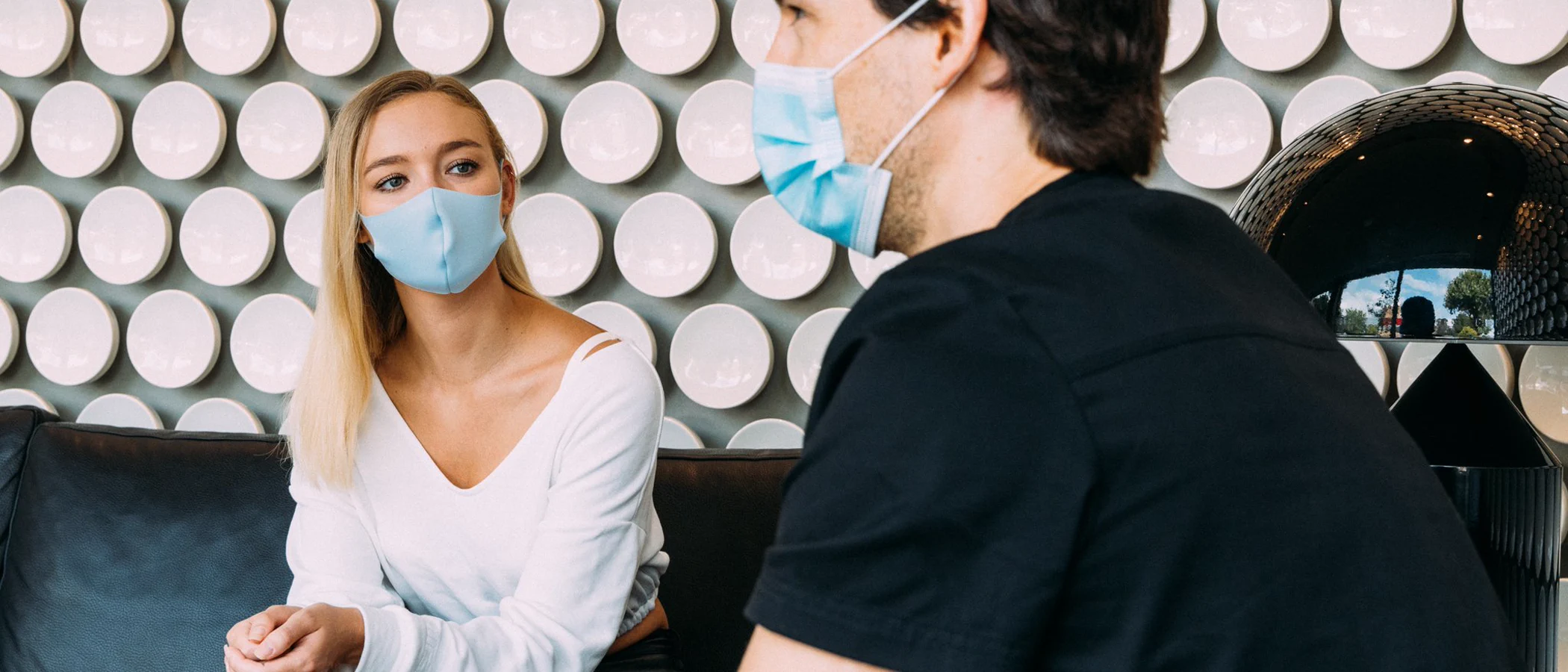 A masked dentist and patient speak in the Maida Smiles consultation lounge.
